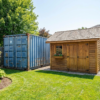 Steel shipping container and wooden shed side by side in a backyard
